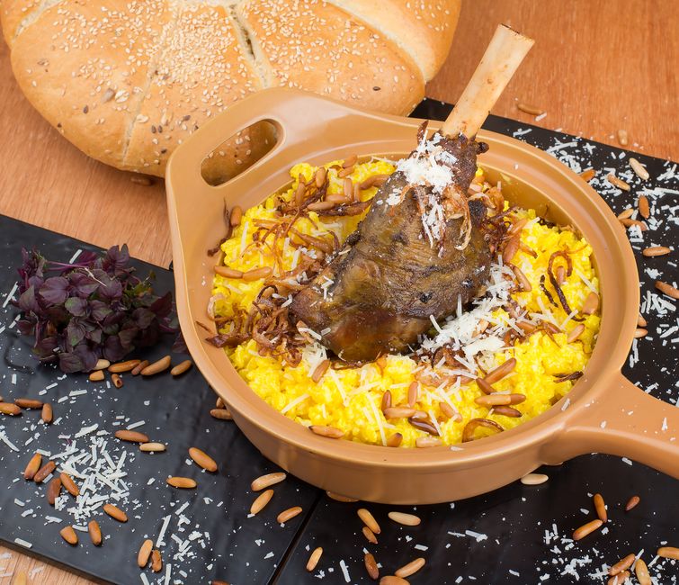 Deliciously plated lamb shank atop saffron risotto garnished with herbs and pine nuts.