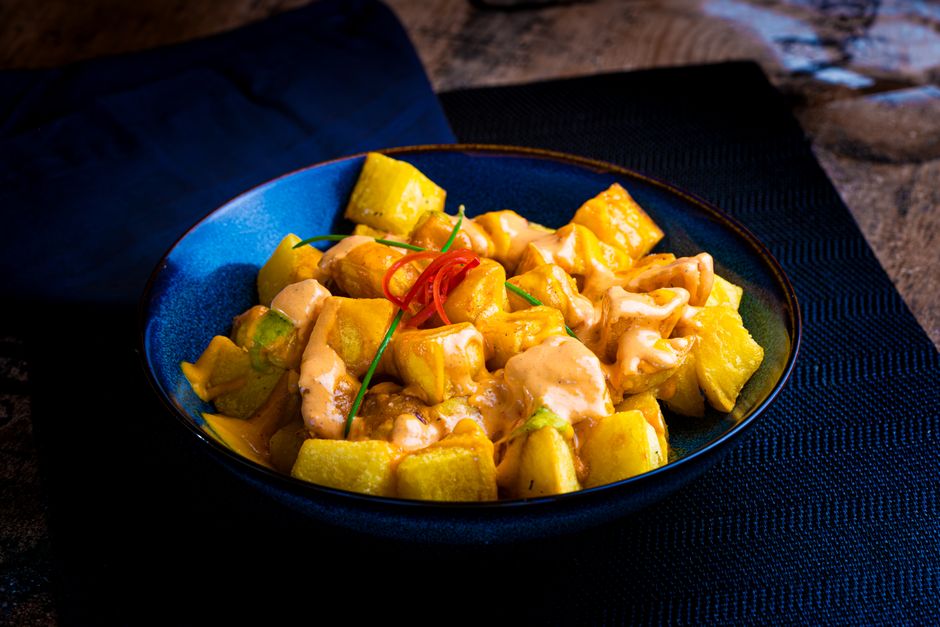 A vibrant dish of patatas bravas with rich sauce on a blue plate, perfect for culinary enthusiasts.
