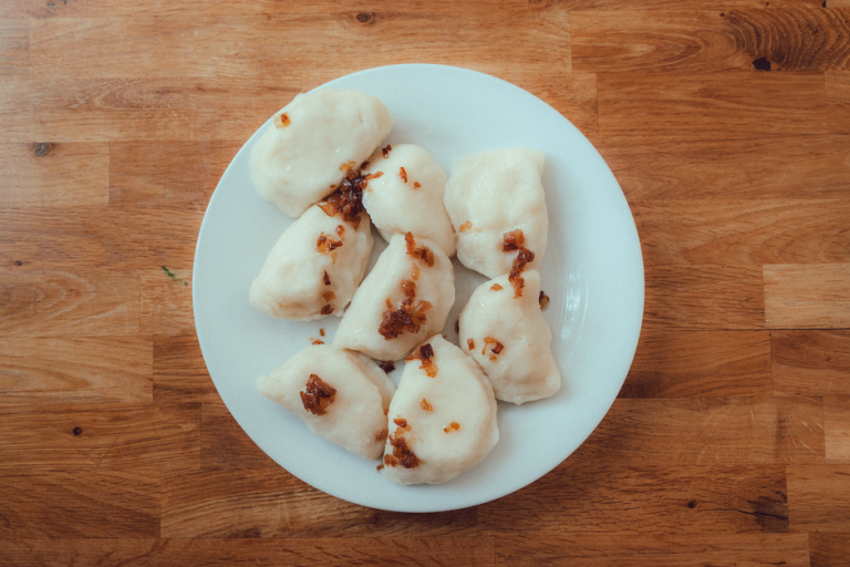 Plate of homemade Polish pierogi with crispy onions on wooden table