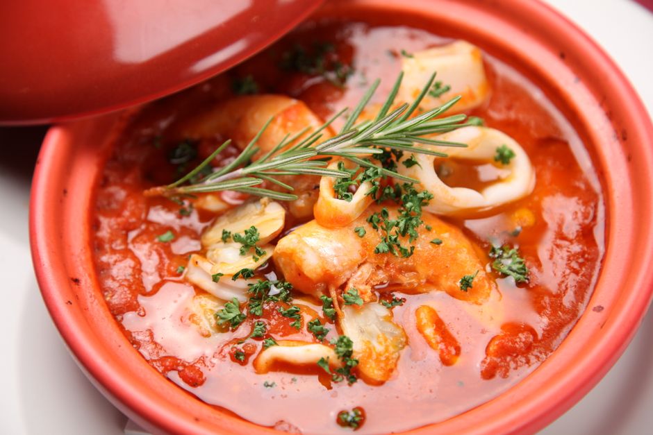 A warm seafood stew with herbs and vibrant tomato sauce served in a ceramic bowl.